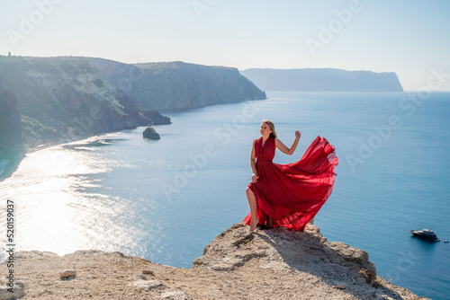 A woman in a red flying dress fluttering in the wind, against the backdrop of the sea.