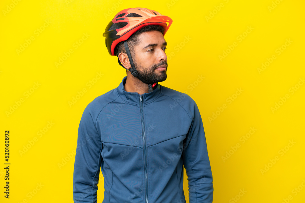Fototapeta premium Young cyclist Brazilian man isolated on yellow background looking to the side