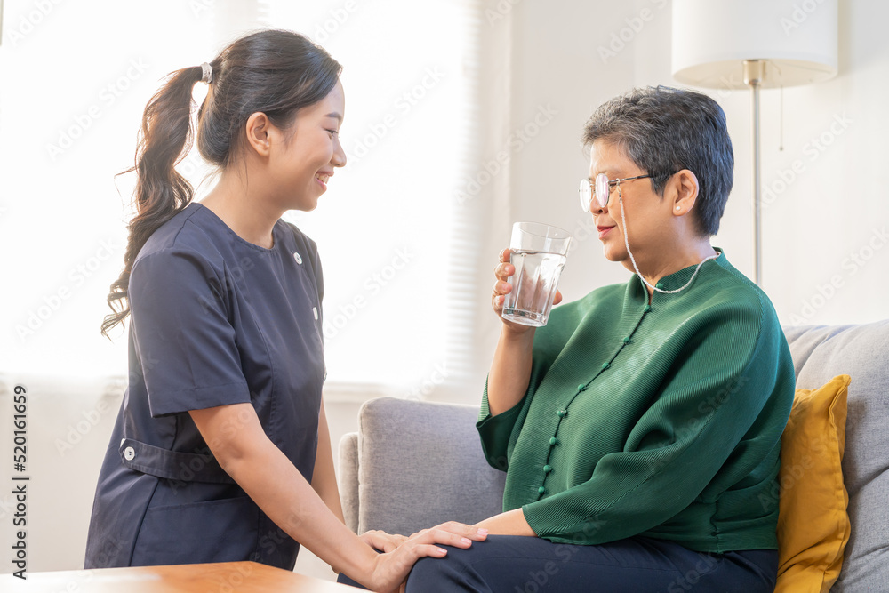 Obraz premium Asian young woman caregiver, carer supporting elderly, aged patient at home, drinking water after take medicine, cure or treatment disease of grandmother after retirement, help support.
