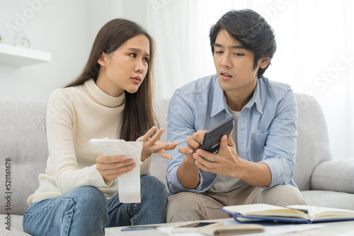Stressed financial owe asian young couple love hand in holding bills, sitting on sofa together, stressed and confused by calculate expense, mortgage or loan. Debt, bankrupt or bankruptcy people.