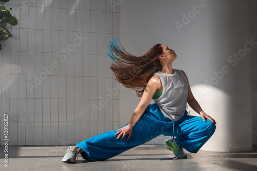 Youth jazz-funk dance style. Young and free, dancing in baggy clothes in a bright white hall. Stylish brunette in blue pants in a dynamic pose