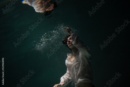 Photo underwater  a guy in a white shirt floundering underwater and reaching for the surface of the water  a man and his reflection. mystical underwater portrait
