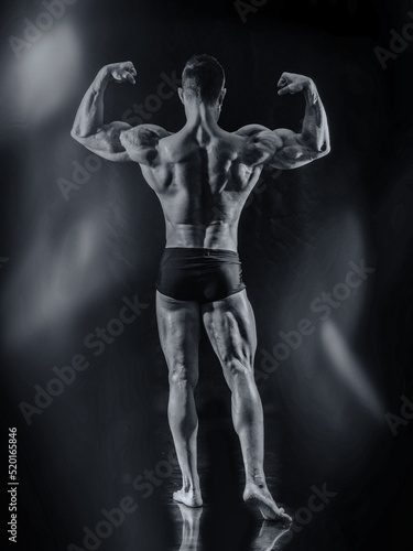 Handsome bodybuilder doing classic back double biceps pose, looking away, on dark background
