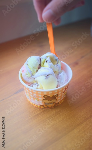 Ice cream on a wooden table. Hand holding an orange spoon.