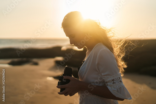 Chica joven al atardecer en la playa haciendo fotos con cámara antigua de carrete de formato medio photo