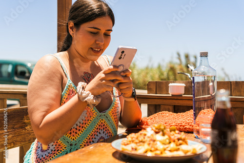 Chica joven guapa feliz en la playa tomando foto sy mirando el telefono movil photo
