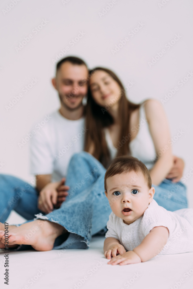 Side view of infant baby toddler in diaper and white bodysuit is crawling on all fours with his legs out, trying to stand up looking at camera over white background. Happy infancy and babyhood concept