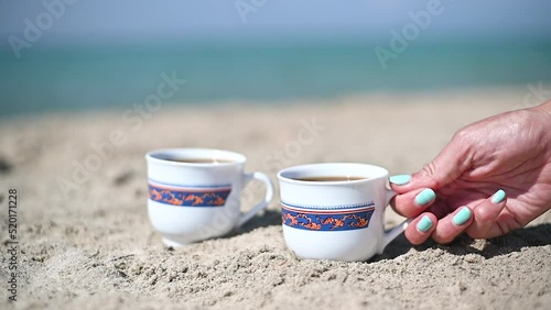 Woman hand taking cup of coffee on the sand beach. Close up slow motion.