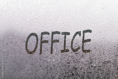 the word office written on night wet window glass close-up with blurred background photo