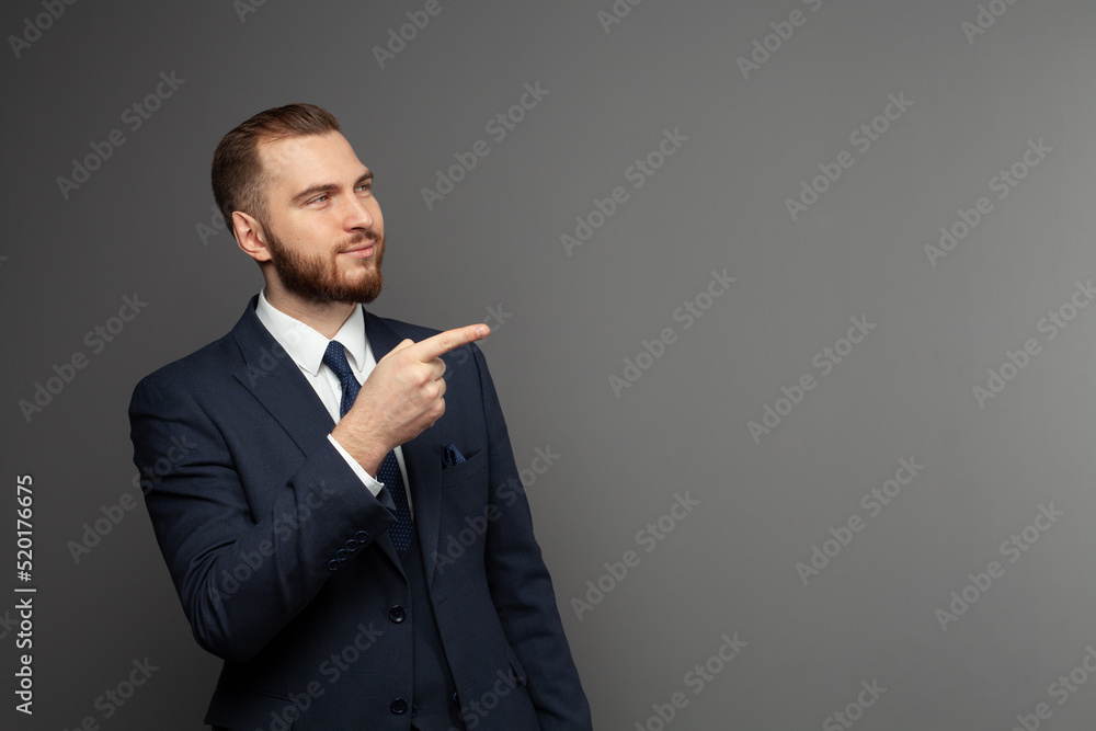 Successful man wearing suit pointing on a copy space on grey background Successful man wearing suit pointing on a copy space on grey background