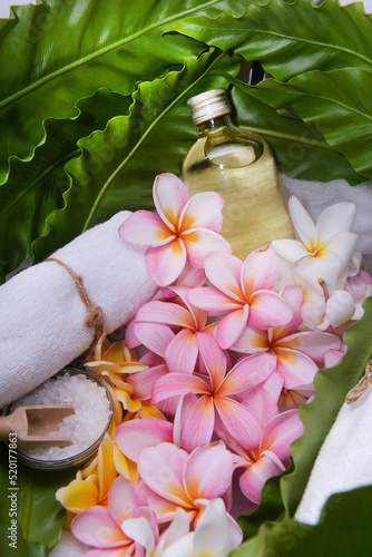 Spa setting with frangipani  bottles of essential oil  salt in bowl  rolled towel on big  leaves  