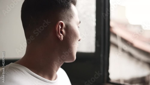 Handsome young latino approaches and looks out the window then gives a look at the camera. 
