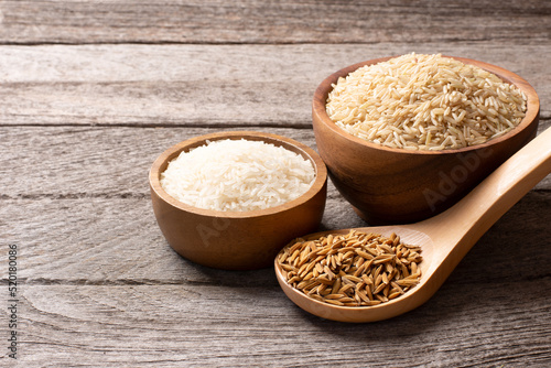 Set of raw rice ; paddy rice, brown coarse rice and white thai jasmine rice in wooden bowl isolated on wooden table background.