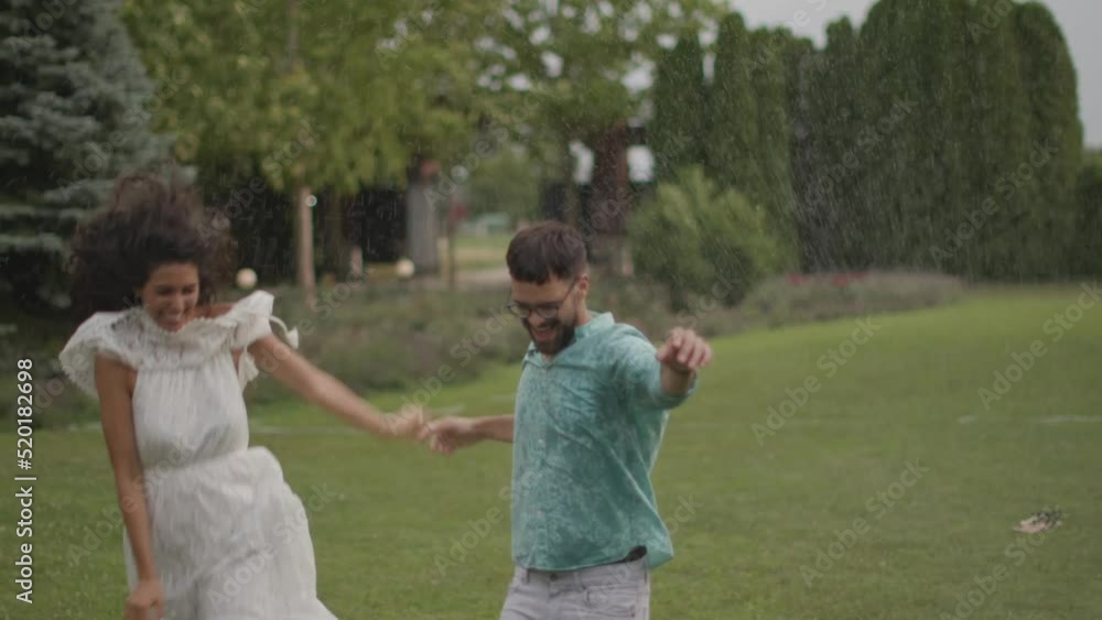 Joyful young couple caught by the sudden sprinkler water in the park Joyful young couple caught by the sudden sprinkler water in the park