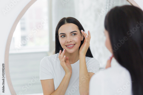 Beautiful young woman in a white t-shirt in the morning looks in the mirror and smiles examining her teeth and makeup