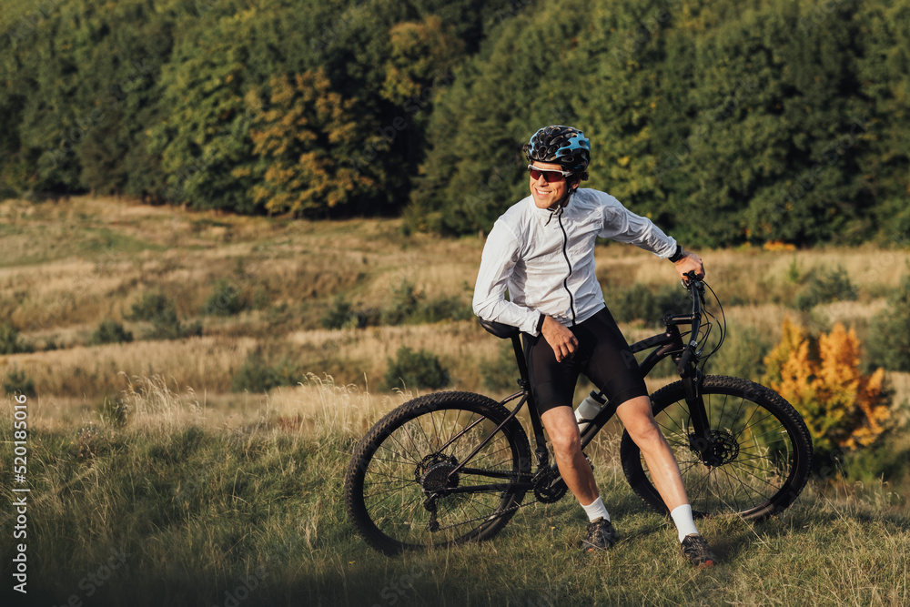 Obraz premium Professional Male Cyclist Leans on His Bike and Adult Man Enjoying Rest During His Ride on Bicycle