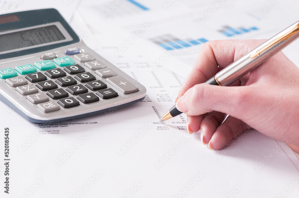Spreadsheet with hand holding pen and calculator in business stock balance sheet Spreadsheet with hand holding pen and calculator in business stock balance sheet