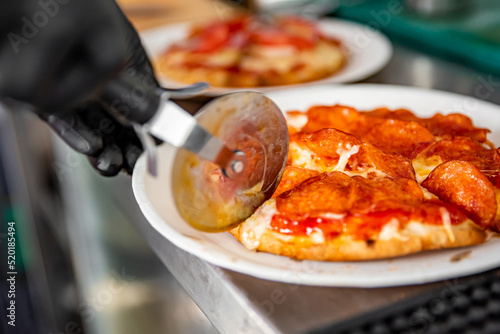 chef hand with cutter cutting mini pita pizza to pieces at pizzeria