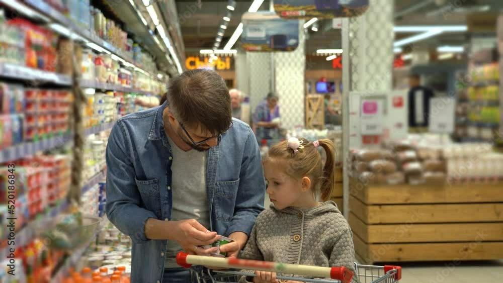 Father and little girl in shopping cart choose yogurt in dairy section in supermarket. Shopping products in store. Buying food, dairy Father and little girl in shopping cart choose yogurt in dairy section in supermarket. Shopping products in store. Buying food, dairy