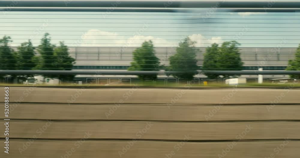 View from fast train commuting near large warehouse parcel distribution center with multiple truck loading unloading goods View from fast train commuting near large warehouse parcel distribution center with multiple truck loading unloading goods