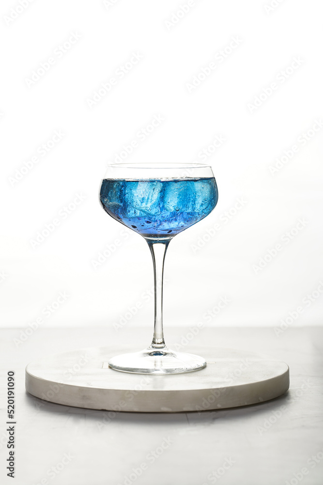 Obraz premium Dark blue drink in a vintage glass for sparkling wine - pea flower tea or blue curacao sirup cocktail, back lighting