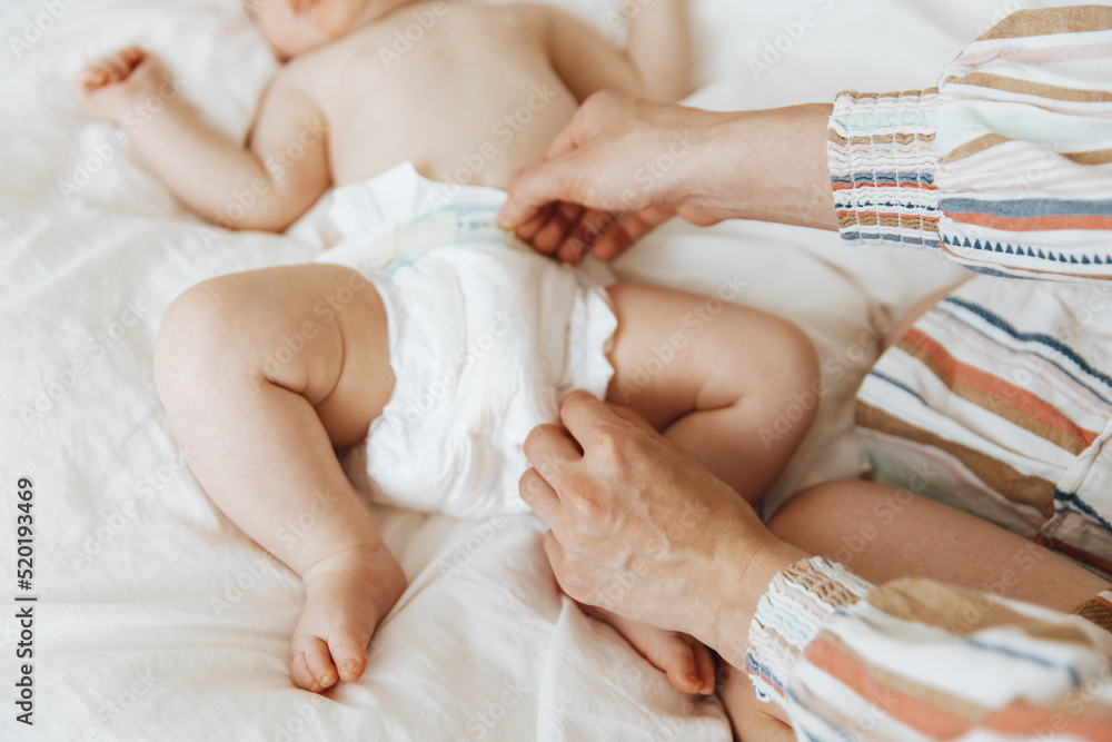 Side view portrait of a mother changing her baby's diaper on the bed, one year old baby concept