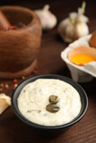 Creamy caper sauce in bowl on wooden table, closeup