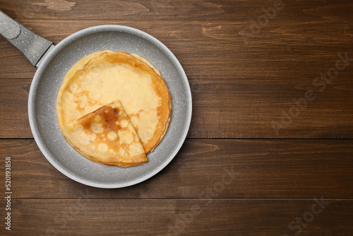 Frying pan with delicious crepes on wooden table, top view. Space for text