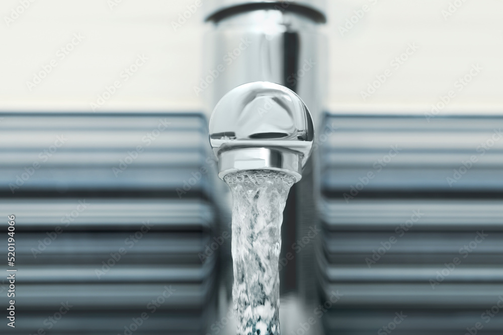 Water flowing from tap on blurred background, closeup Water flowing from tap on blurred background, closeup
