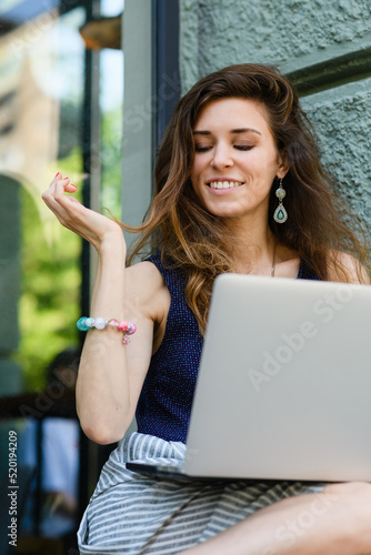 Young attractive woman with laptop sits on the windowsill outdoors.