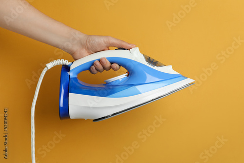 Woman holding modern iron on orange background, closeup