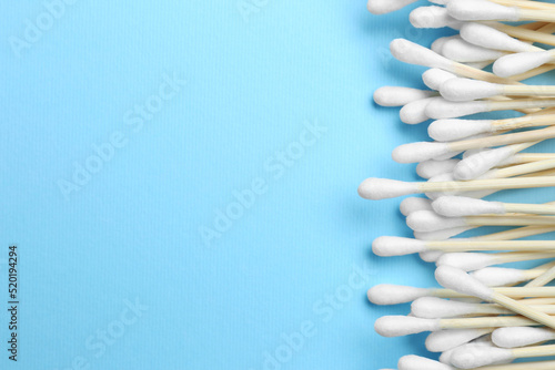 Many cotton buds on light blue background, flat lay. Space for text