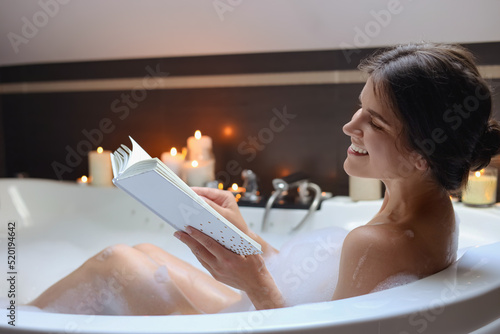 Fotografia Young woman reading book while taking bubble bath