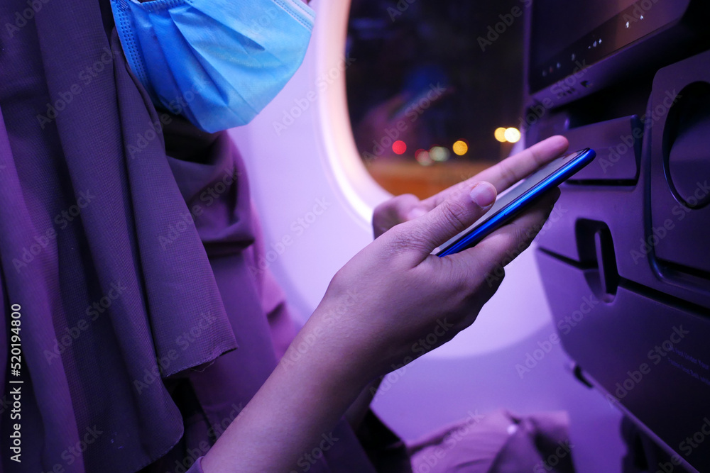 women with a face mask using smart phone sitting on airplane seats in the cabin