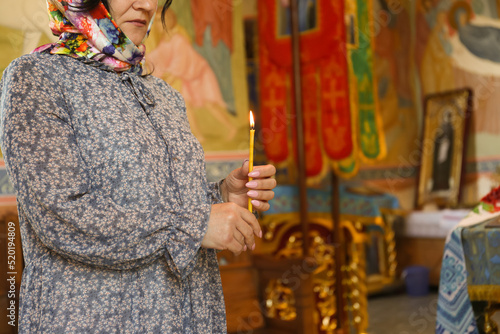 Mature woman holding candle in church, closeup. Space for text