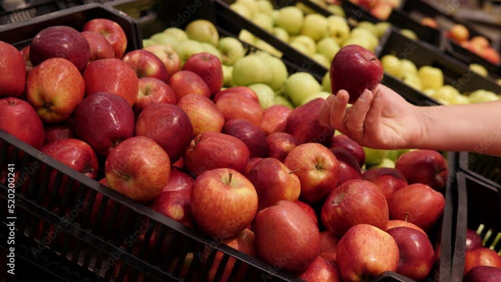 Close-up of a woman choosing red apples in a supermarket. A woman's hand with a red apple in a grocery store. Close-up of a woman choosing red apples in a supermarket. A woman's hand with a red apple in a grocery store.