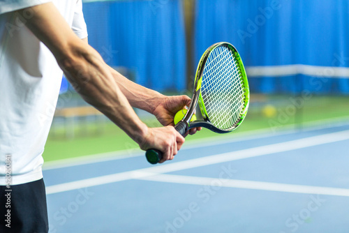 A man in a sports uniform holds a racket and a ball in his hands and is about to serve. Hands close up