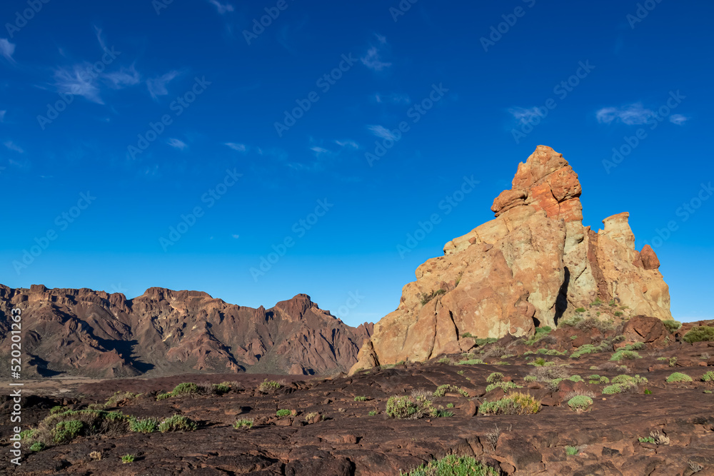Scenic view on unique rock formation at Roques de Garcia, Mount Teide National Park, Tenerife, Canary Islands, Spain, Europe. Hiking trail over barren volcanic stone terrain. Blue sky background