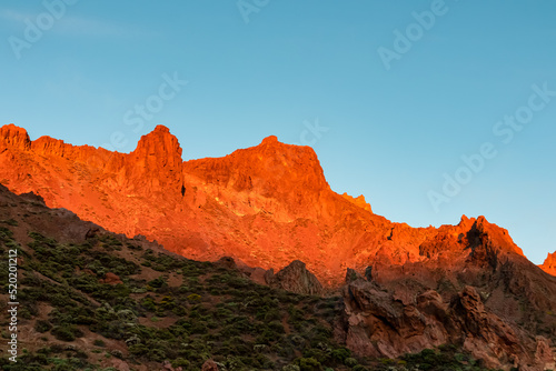 Scenic view on rock formations during sunrise near volcano Pico del Teide  Mount Teide National Park  Tenerife  Canary Islands  Spain  Europe. First sunbeams touching mountain peaks turning fire red