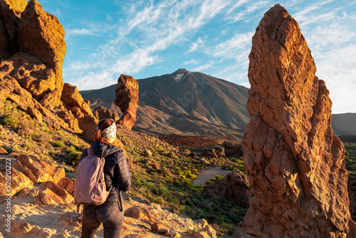 Woman with backpack hiking with scenic golden hour sunrise morning view on unique rock formation Roque Cinchado, Roques de Garcia, Tenerife, Canary Island, Spain, Europe. Pico del Teide volcano summit photo