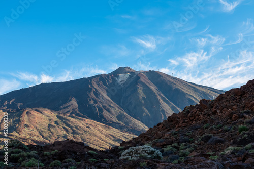 Panoramic view on volcano Pico del Teide after sunrise, Mount El Teide National Park, Tenerife, Canary Islands, Spain, Europe. Volcanic terrain. Looking from Paradores Canadas. Hiking trail in shadow