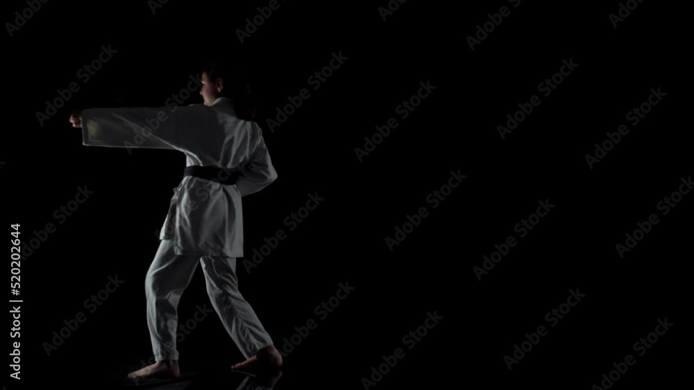 Young girl wearing kimono and practicing karate against black background Young girl wearing kimono and practicing karate against black background