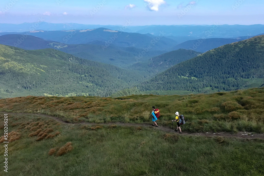 Two hikers with backpacks are walking along mountain range in Carpathian mountains