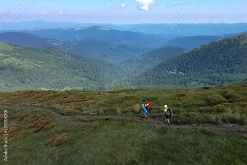 Two hikers with backpacks are walking along mountain range in Carpathian mountains