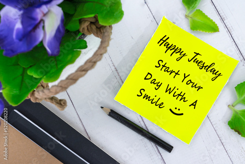 Motivational quote on yellow note with flowers on wooden background