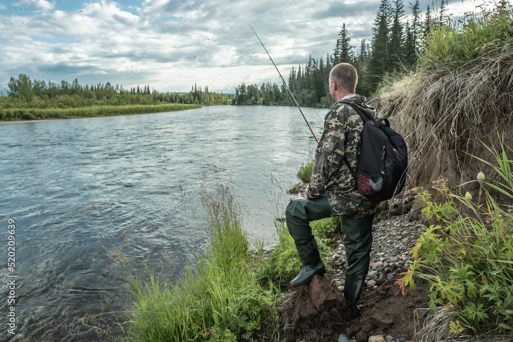 Male fisherman is standing on the riverbank with a fishing rod in his hands and catching fish. Calm outdoor recreation Male fisherman is standing on the riverbank with a fishing rod in his hands and catching fish. Calm outdoor recreation