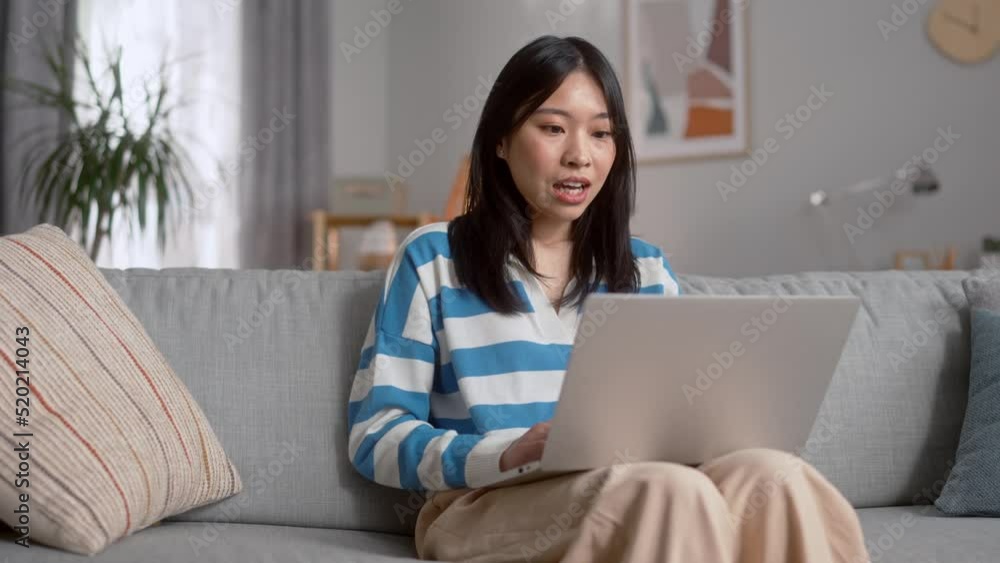 Attractive young asian female having video chat on modern laptop at home. Happy dark haired woman waving hello greetings and talking during online conversation. Attractive young asian female having video chat on modern laptop at home. Happy dark haired woman waving hello greetings and talking during online conversation.