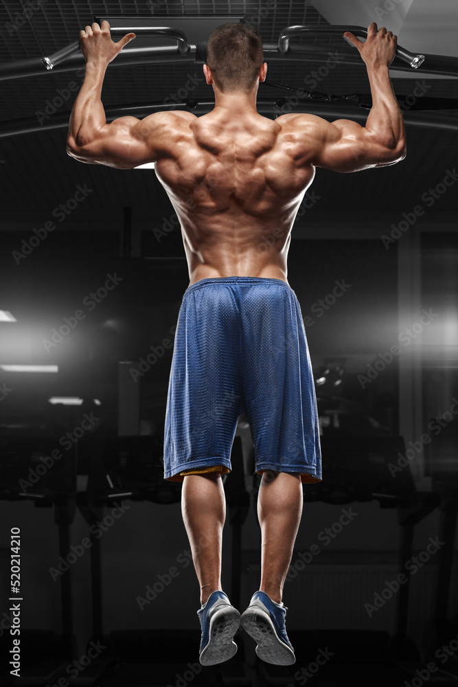 Muscular man doing pull up on horizontal bar in gym, working out