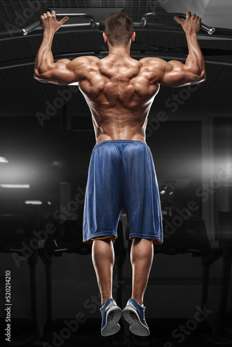 Muscular man doing pull up on horizontal bar in gym, working out. Strong fitness male pulling up, showing back