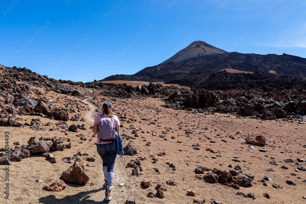 Woman with backpack on volcanic desert terrain hiking trail leading to summit volcano Pico del Teide, Mount Teide National Park, Tenerife, Canary Islands, Spain, Europe. Solidified lava, ash, pumice